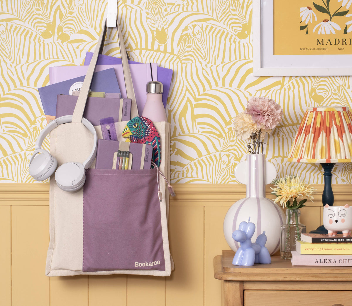 Purple tote bag with stationery items against a yellow patterned wall.