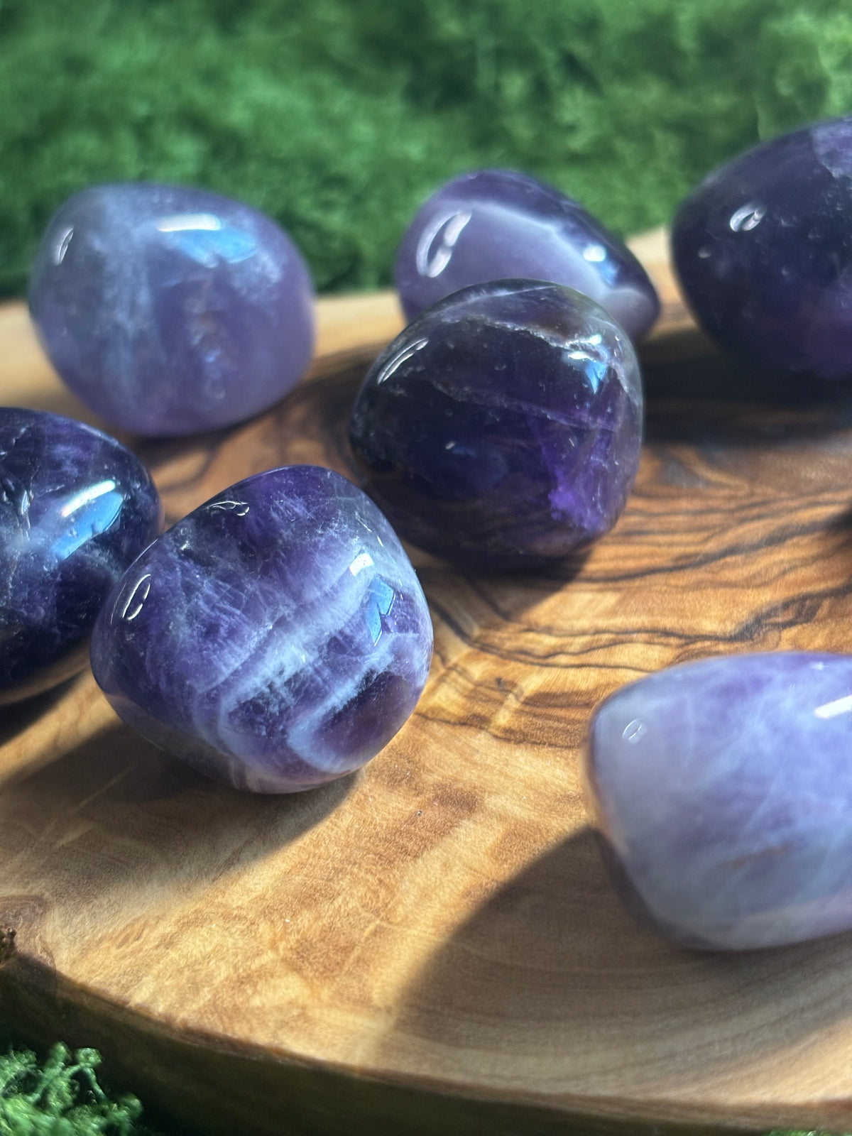 Natural polished amethyst tumbled stones in purple and lavender tones displayed on a wooden board.